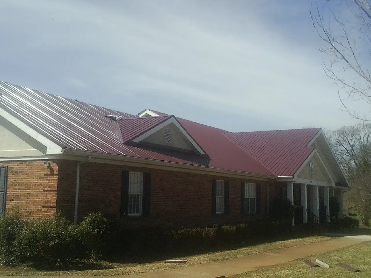 Red metal roof with gabled entries on a long brick building, from a Hail Damage Roof Repair job in San Lorenzo