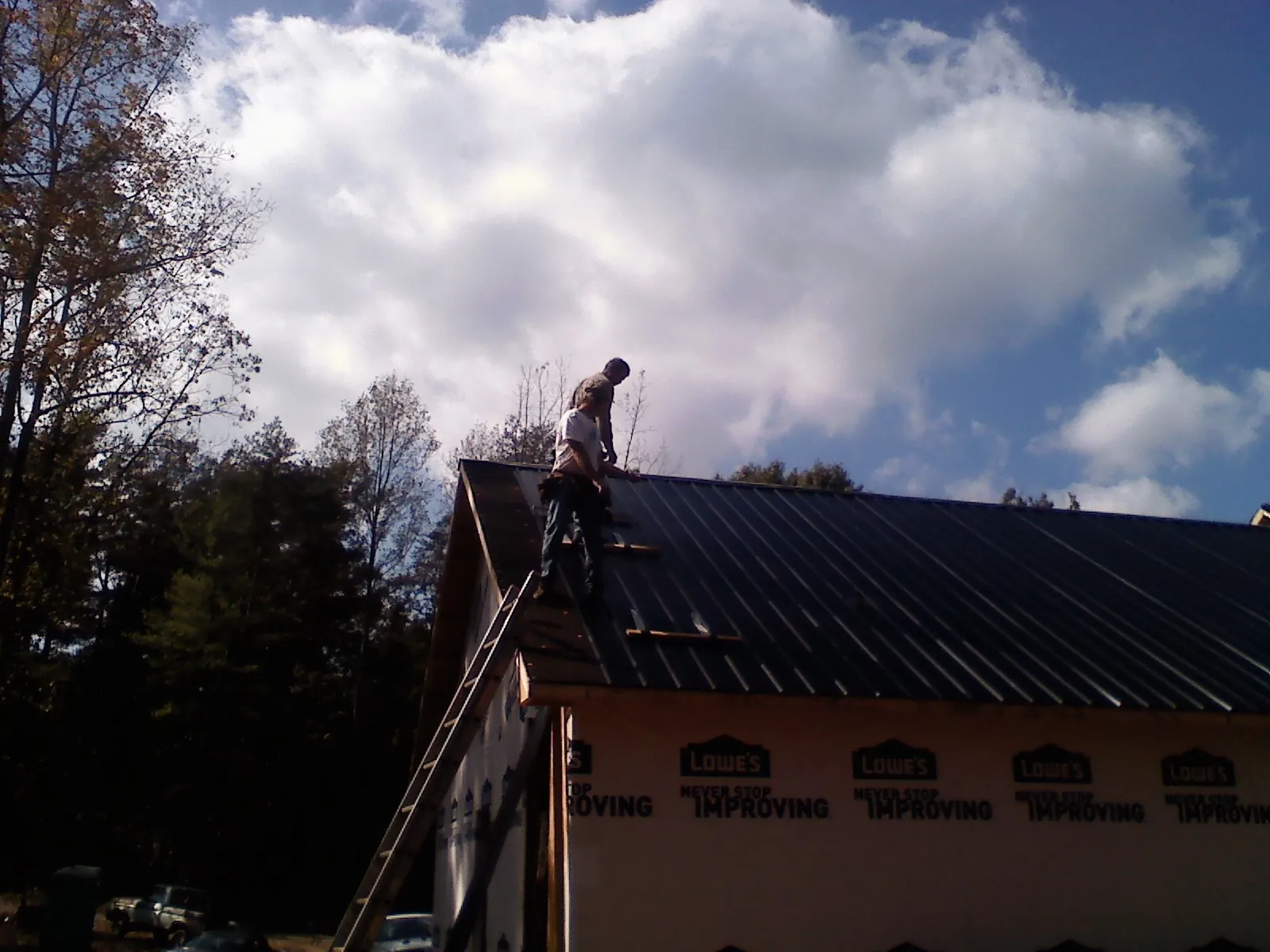 Roofer fastening dark metal panels high against a cloudy sky, from a Roof Inspection job in San Lorenzo