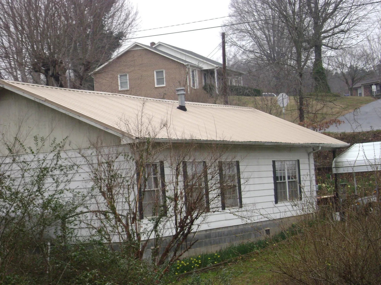 Tan metal roof on a white sided house set into a hillside — Commercial Roofing by Roofing Brothers in San Lorenzo